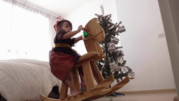 带长凳玩具的亚洲可爱女孩正在家里玩圣诞树装饰
