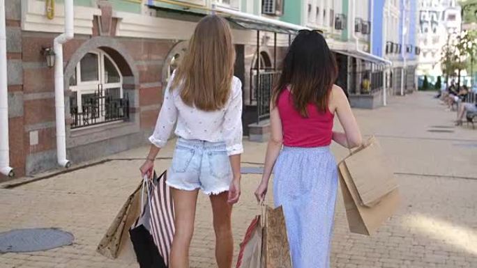 后视图。两个漂亮的女人在成功购物后走上街头，用纸袋4k和慢动作