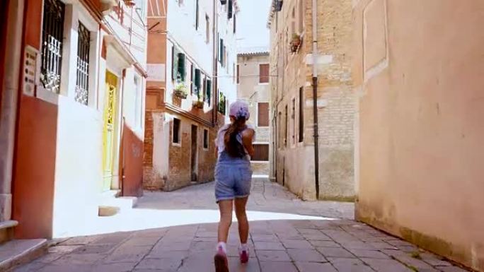 意大利威尼斯-2018年7月7日: 沿着威尼斯的一条狭窄街道，在老房子之间，一个十几岁的女孩，一个孩