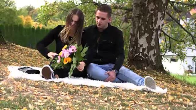 一对年轻夫妇坐在秋天公园的白色床罩上