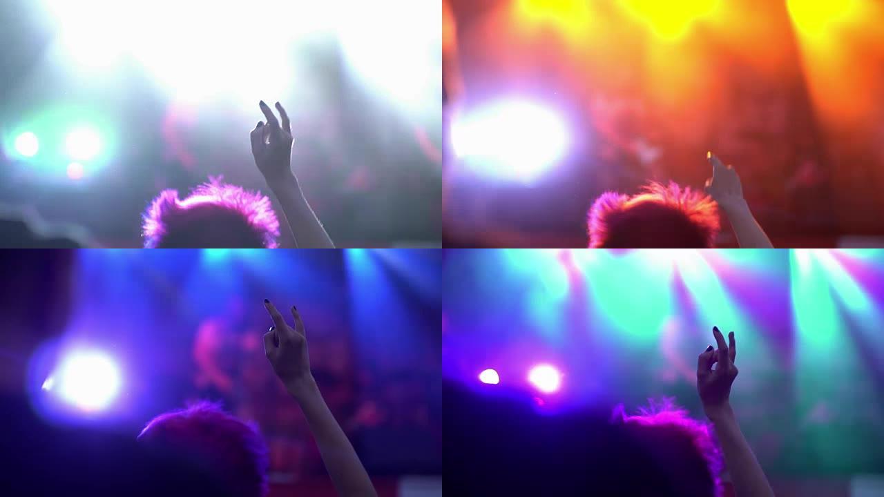 夜间摇滚音乐会。人们欢呼雀跃，举起手来，在频闪的舞台灯光下齐声拍手。手部特写向上，显示摇滚标志。舞台