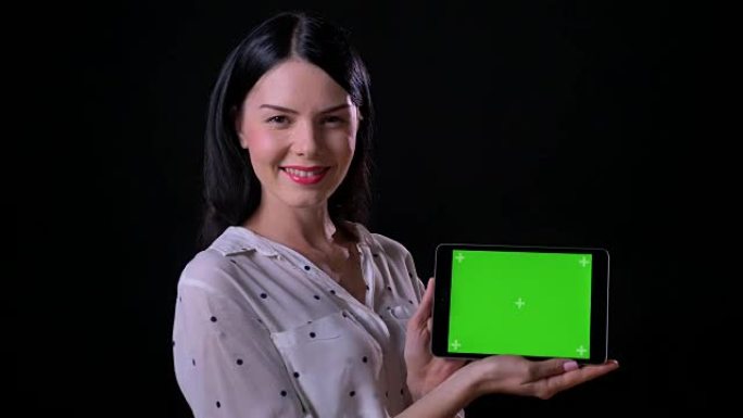 美丽迷人的年轻女子展示色度和微笑的平板电脑，孤立在黑色背景上