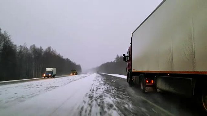 在恶劣的下雪大风天气中，重型货车在高速公路上行驶。通过挡风玻璃的视图-驾驶员的角度。移动视频。