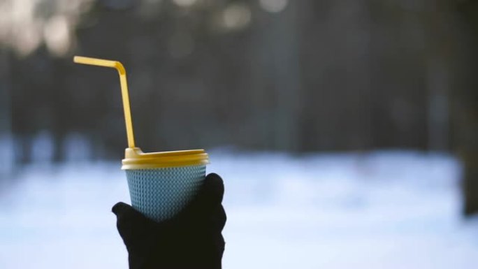 咖啡。一只手拿着一杯咖啡，背景是白雪覆盖的公园。
