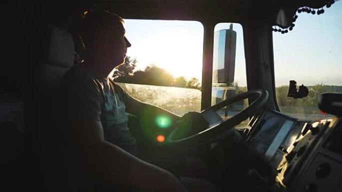 男子驾驶卡车，仔细观察道路。白种人在日落背景下穿越乡村。驾驶室内卡车司机的简介。侧视图慢动作特写