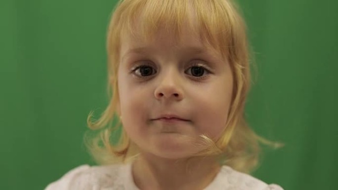 快乐的三岁女孩纠正发型。可爱的金发孩子。棕色的眼睛。绿屏