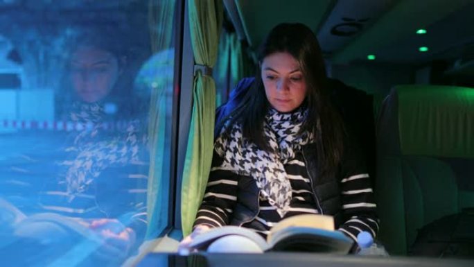 晚上乘公共汽车旅行时，偷拍的4k视频。晚上，女孩在窗户旁边的行驶车辆上读故事