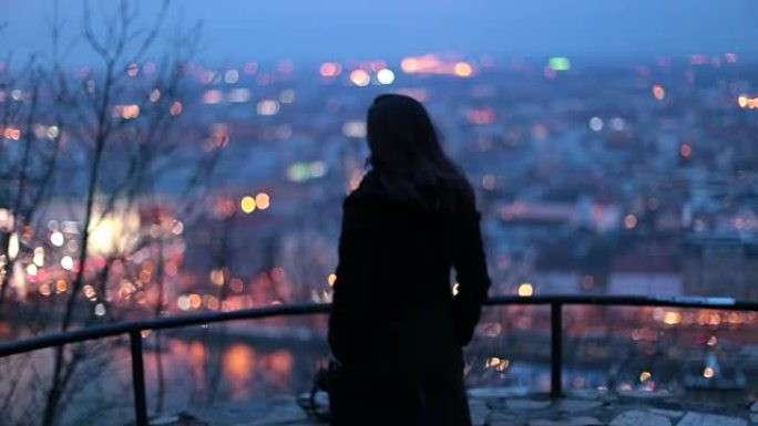 女人在晚上看着城市景观。沉思的人在晚上看城市景观时思考生活