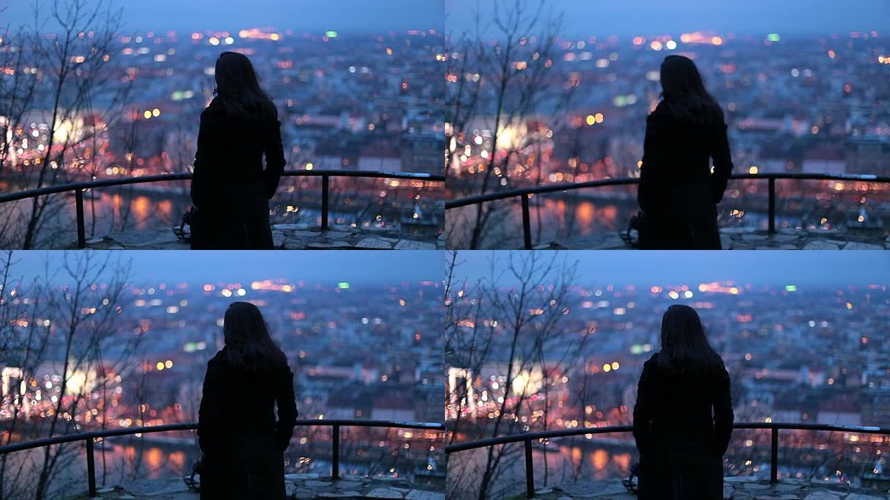 女人在晚上看着城市景观。沉思的人在晚上看城市景观时思考生活