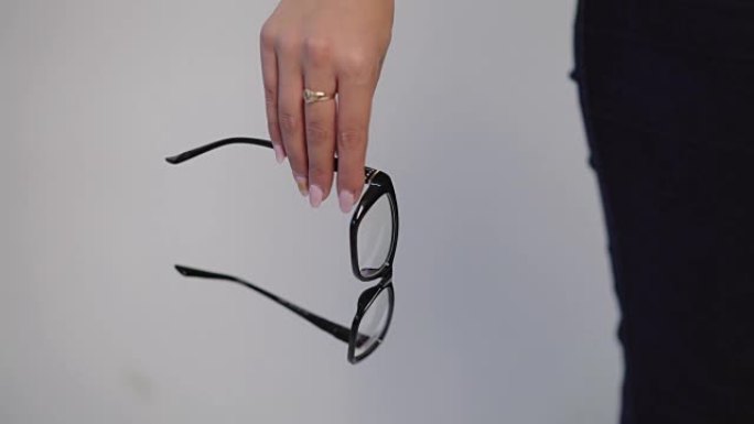 女性手握着灰色背景黑框眼镜模型