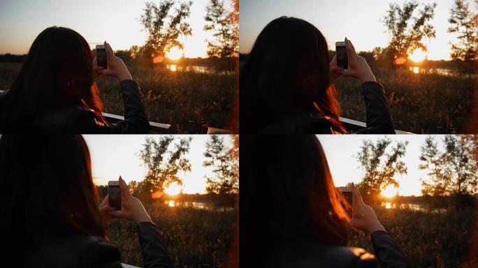 年轻女子在智能手机上拍摄日落照片。