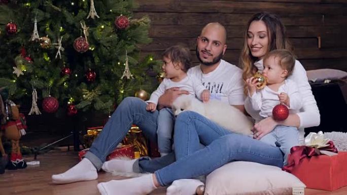 家庭圣诞节，父母和孩子与小狗坐在一起，看着背景圣诞树上的相机