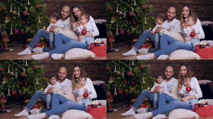 家庭圣诞节，父母和孩子与小狗坐在一起，看着背景圣诞树上的相机
