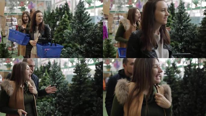 一群朋友在超市的圣诞拍卖会上，在人造圣诞树中选择圣诞装饰品。
