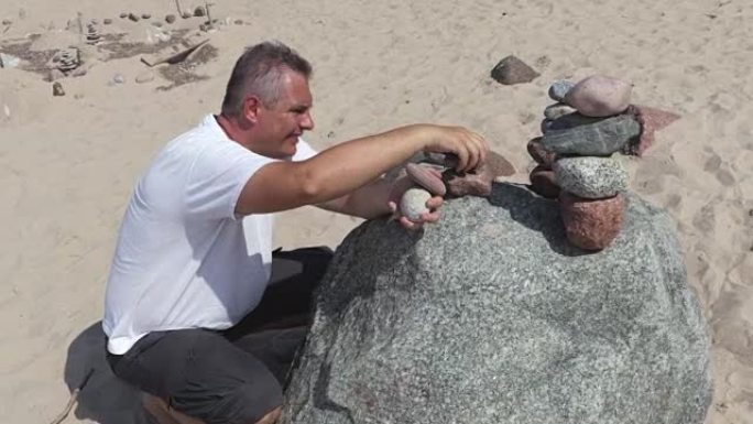男人在夏天的海滩上建造了一个平衡的石头金字塔
