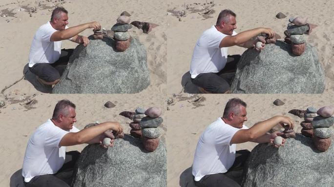 男人在夏天的海滩上建造了一个平衡的石头金字塔