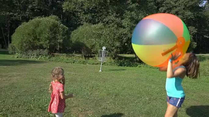 两个不同年龄的可爱的女孩玩一个巨大的彩色彩虹充气球。