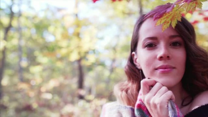 在秋天的森林里，黑发女人微笑着对着镜头的滑动肖像。