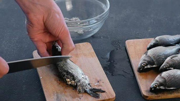 男人从木板上的鳞片上清洗鲤鱼。特写手。煮一条鱼。