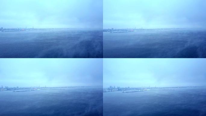 空中揭示城市和海洋拍摄。雾蒙蒙的寒冷冬天的大海。蓝色的海洋背景，光滑的云层和美丽的神秘纹理。