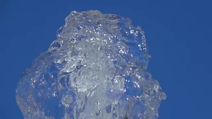 一小点清澈的冰水。夏天，在蓝天背景下，公园阳光充足的喷泉里洒水的特写镜头。喷泉的水流在空气中飞起，飞