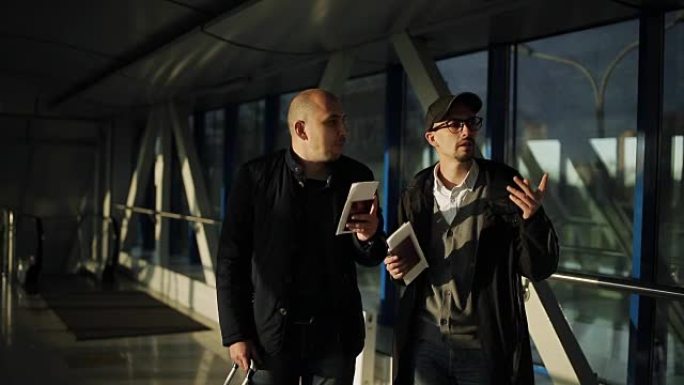 机场的两名男子沿着走廊走，寻找航班上的接待处。
