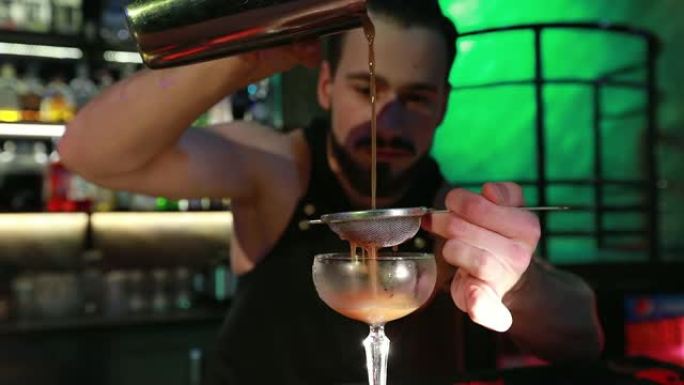 大胡子的酒保将准备好的鸡尾酒倒入玻璃杯中。