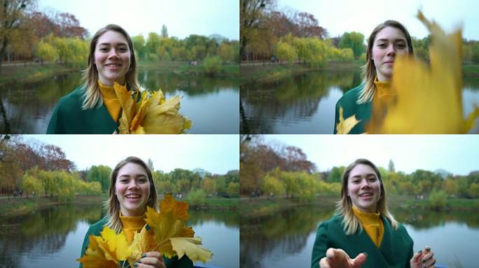 年轻的女孩向相机扔黄色的叶子。穿着绿色外套的金发少女。