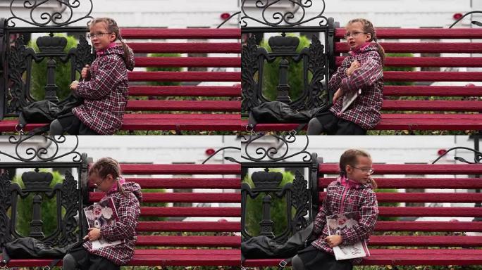 戴眼镜的女童在他的相册中画了一幅画。一个女孩坐在公园的长椅上。秋天的日子。
