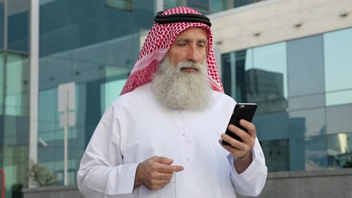 在城市里，一位留着胡子的阿拉伯老年男子正在用智能手机交流