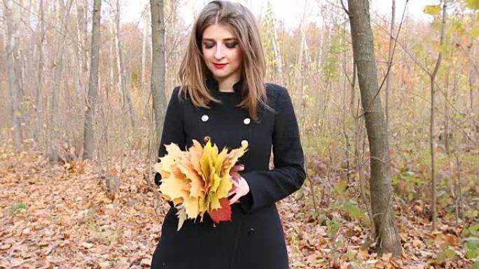穿着黑色外套的年轻女子拿着一束秋叶
