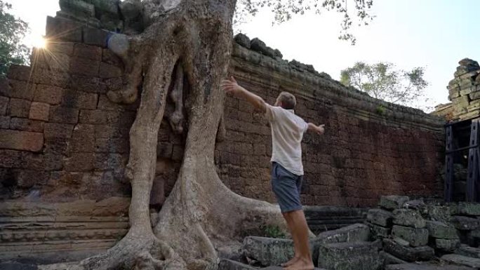 在亚洲旅行的男子参观柬埔寨的古老寺庙，站在树旁张开双臂，以自由和积极的情感