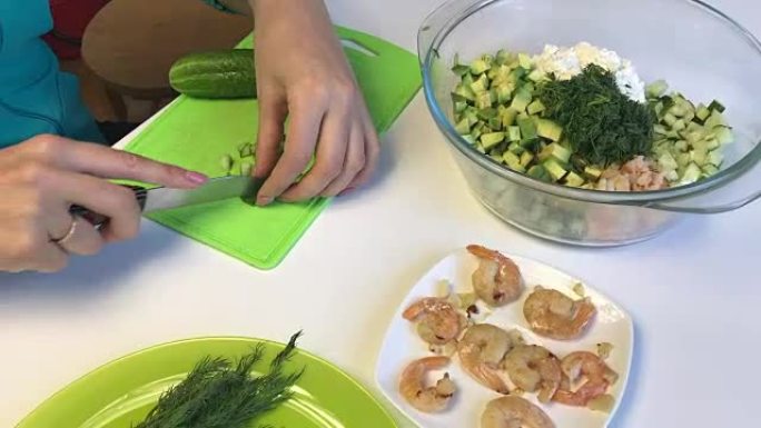 桌子的表面上站着凝乳团，蔬菜和虾，用于烹饪。女人切黄瓜。