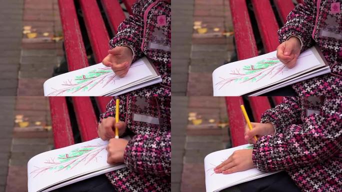 戴眼镜的女童在他的相册中画了一幅画。一个女孩坐在公园的长椅上。秋天的日子。