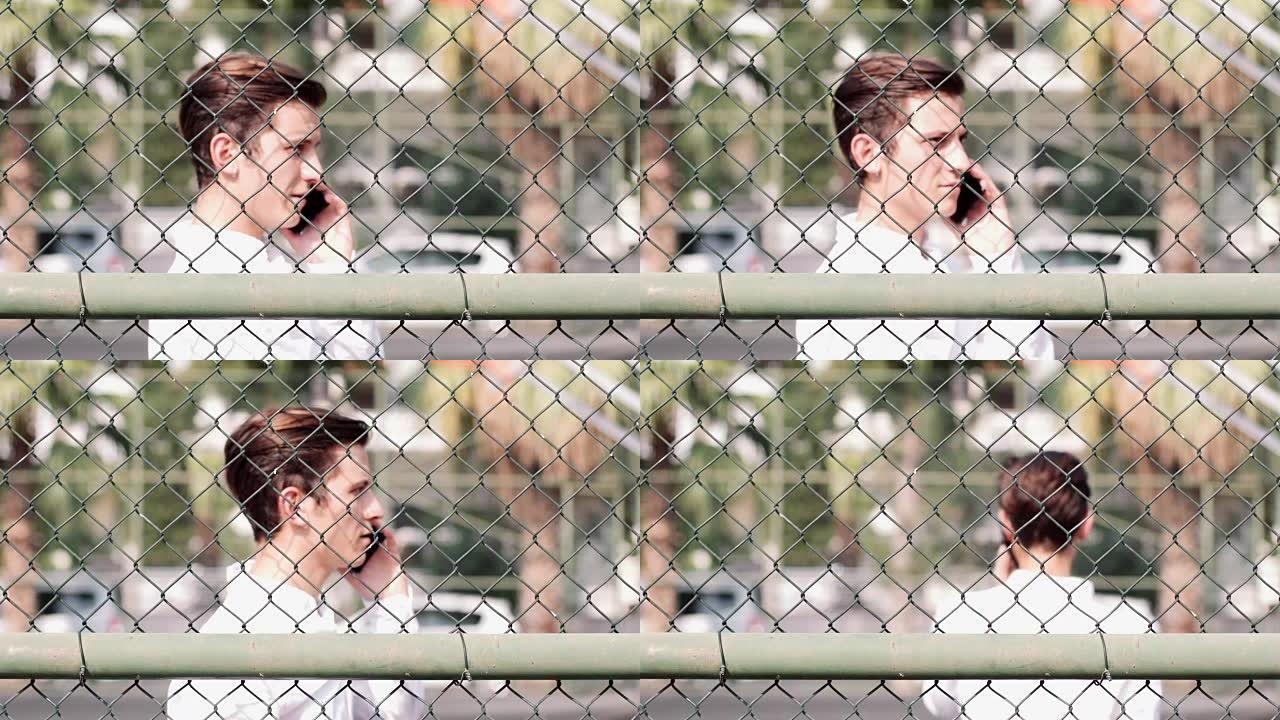 一个迷人的年轻人在篱笆后面用电话聊天的肖像