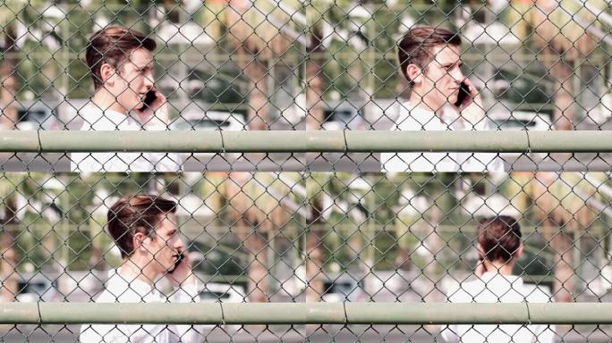 一个迷人的年轻人在篱笆后面用电话聊天的肖像