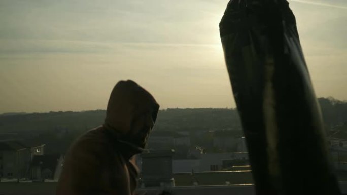 带战斗手套的拳击手站在日落时的警卫拳袋中，特写镜头，城市，运动员练习，力量训练，强壮的家伙努力锻炼，