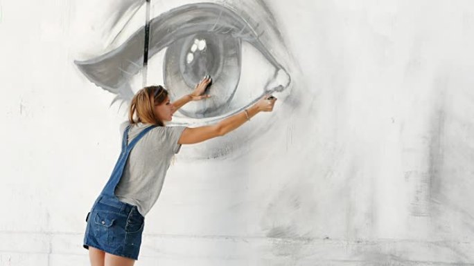 涂鸦艺术家在街头墙上用油漆画出美丽的女人和眼睛的脸。用刷子工作的女性。城市户外艺术概念。慢动作