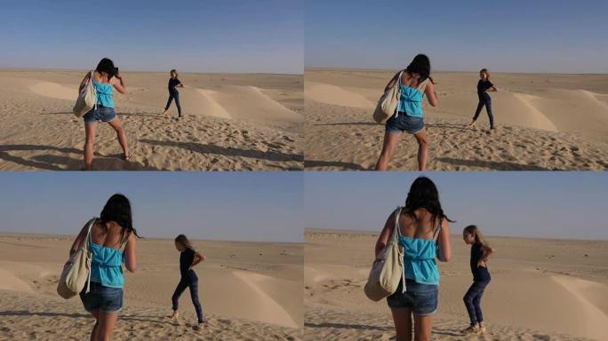 年轻的母亲在沙质沙漠背景下用手机给女儿拍照