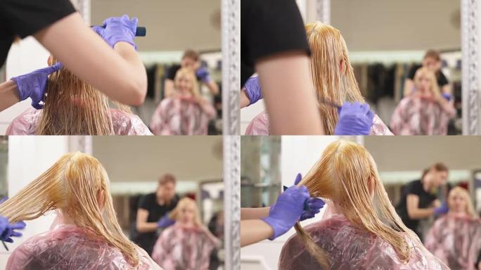 金发女郎正坐在镜头前，染上头发。理发师把它梳到一定长度。这个女人用手指显示了一些东西。他们的反射在他