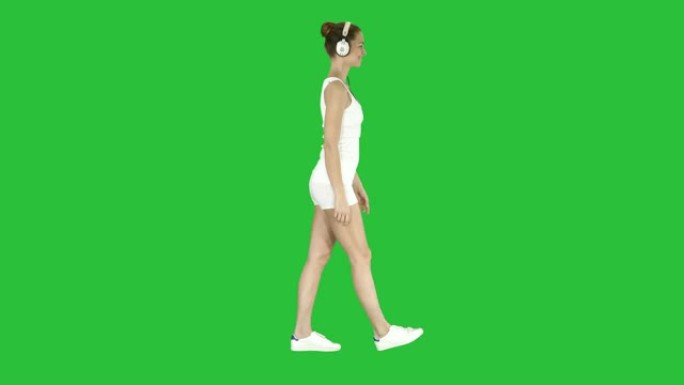 穿着白衬衫的女人用耳机听音乐，在绿色屏幕上行走，色度键
