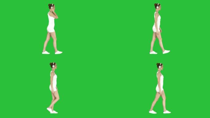 穿着白衬衫的女人用耳机听音乐，在绿色屏幕上行走，色度键