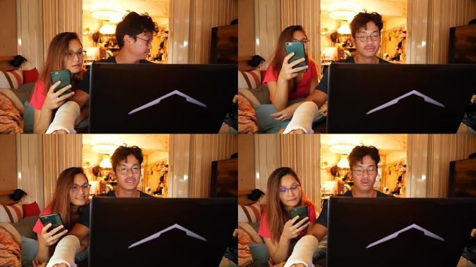年轻的亚洲男人和女人，在餐桌上与可爱的黑色法国斗牛犬一起工作的笔记本电脑在卧室里，戴着眼镜，微笑着。