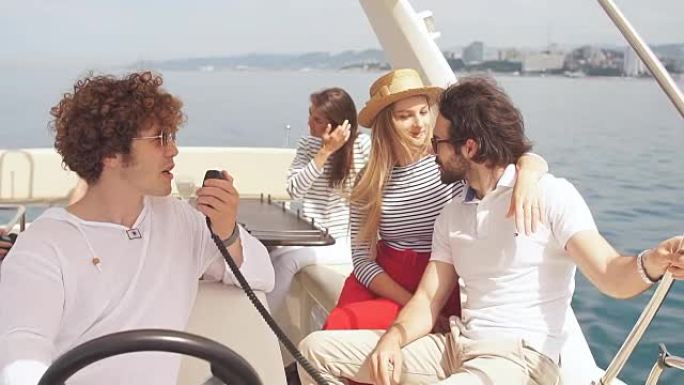 年轻的卷发男子在海船上航行，与他快乐的朋友，坐在旁边的男孩和女孩一起航行，享受新鲜的海风