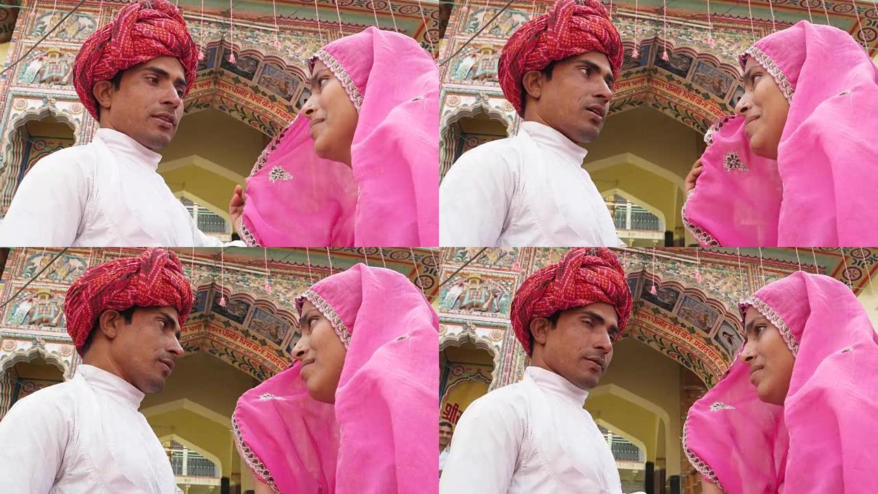 印度拉贾斯坦邦普什卡的一座寺庙外，穿着粉红色纱丽的美丽女子和戴着红色头巾的迷人男子