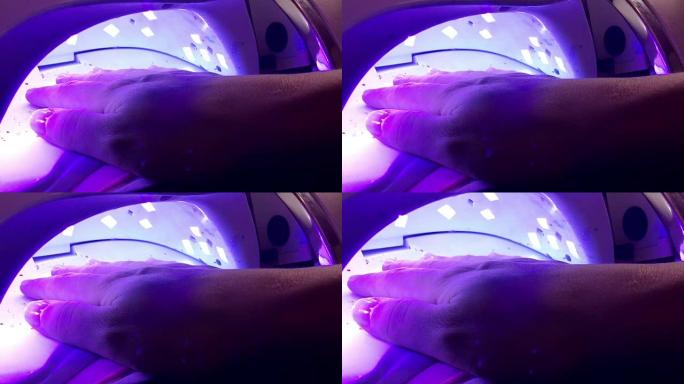 女人在水疗沙龙的紫外线灯里烘干指甲油。
