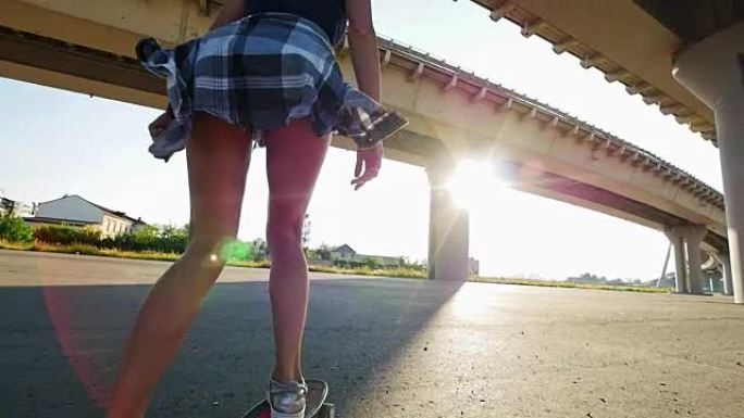 美丽的女孩在阳光下，在腿的框架下，在桥下骑滑板