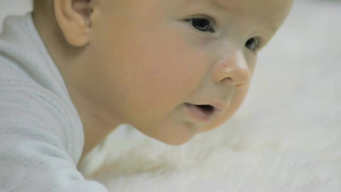 一个刚出生的男孩的特写镜头，躺在白色毯子上的肚子上，微笑着慢动作。