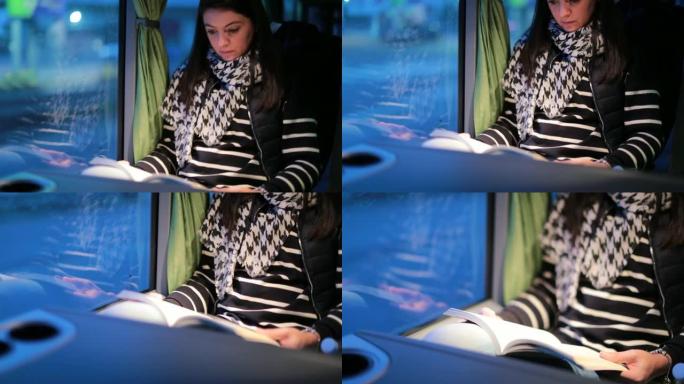 晚上乘公共汽车旅行时低头看书的女人。路过窗户的风景