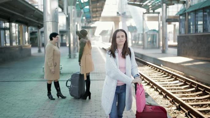人们带着旅行包在铁路站台火车站，等待火车的到来。前景中的一个迷人女孩。